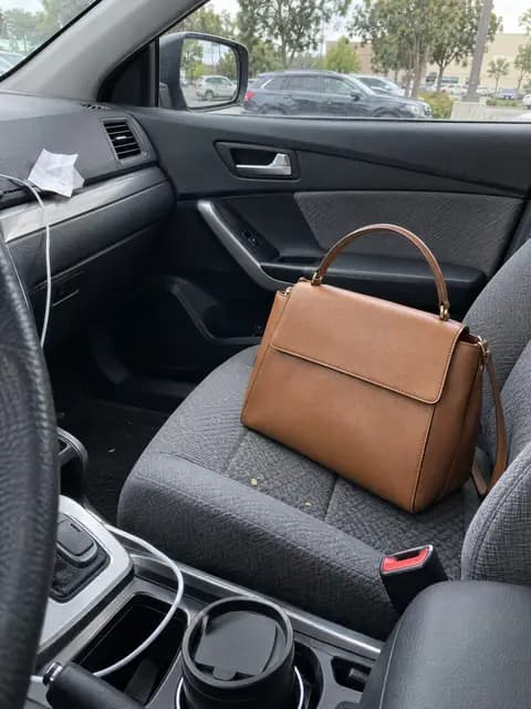 A tan leather handbag on a car seat, shot on a phone